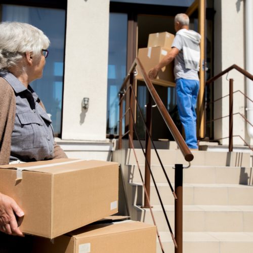 Portrait of modern senior couple unloading cardboard boxes while moving to new house, copy space